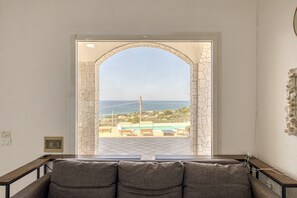 Ein Zimmer mit Blick auf einen Pool und das Meer, ein Steinbogen und ein Sofa.
