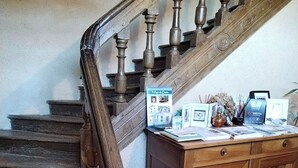 Una scala in legno con corrimano, un mobiletto di legno con diversi oggetti sopra e un pavimento piastrellato.