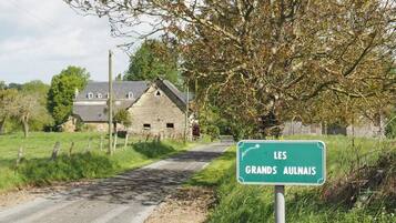 A rural road with a sign for 'LES GRANDS AULAIS' and a stone house in the background.