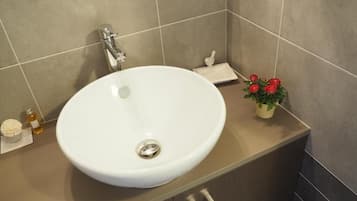 Et badeværelse med en hvid vask, en lille plante og en sæbedispenser.