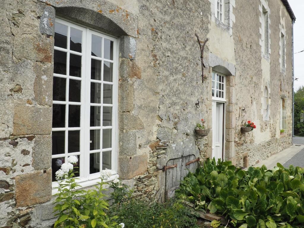 A stone building with a large window, a door, and a small garden area with plants.