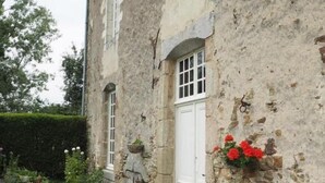 Un edificio in pietra con una porta bianca, una piccola finestra e una fioriera con fiori rossi.