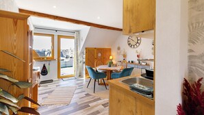 A modern kitchen with wooden cabinets, a dining area with blue chairs, and a view through a glass door. - Apartment 'Für 2 Personen 43 M²' with Balcony and Wi-Fi (Mendig)