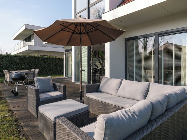 A modern outdoor seating area with wicker furniture and a large umbrella.
