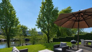 Un patio con mobiliario exterior, una parrilla y vistas a un lago.