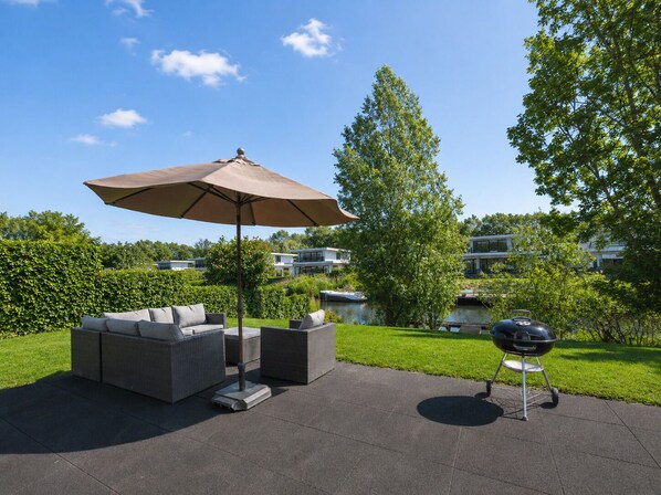 Eine Terrasse mit Gartenmöbeln, einem Grill und Blick auf eine Wohngegend.
