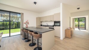 A modern kitchen with a large island, bar stools, and a view of the outdoors. - Luxury 10-person villa on the water with hot tub, private jetty, spacious terrace and 4 bedrooms. Located at Villa Resort Harderwold, near Harderwijk and the Veluwemeer! (Zeewolde)