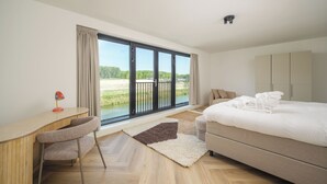 A modern hotel room with a large window, a bed, a desk, and a chair. - Luxury 10-person villa on the water with hot tub, private jetty, spacious terrace and 4 bedrooms. Located at Villa Resort Harderwold, near Harderwijk and the Veluwemeer! (Zeewolde)