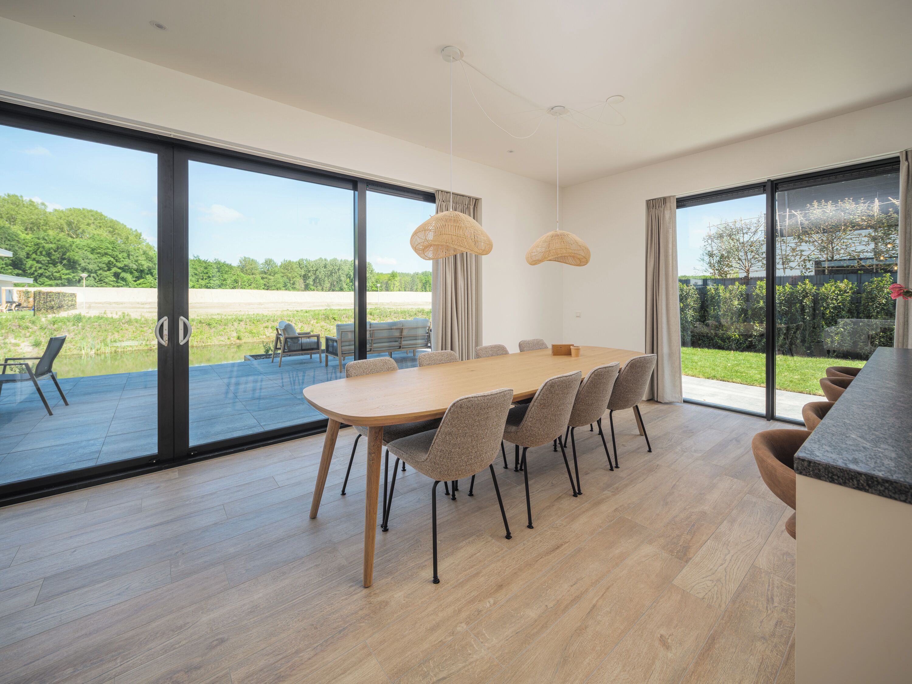 Un espace repas moderne, doté d’une grande table, de chaises et offrant une vue sur l’extérieur.