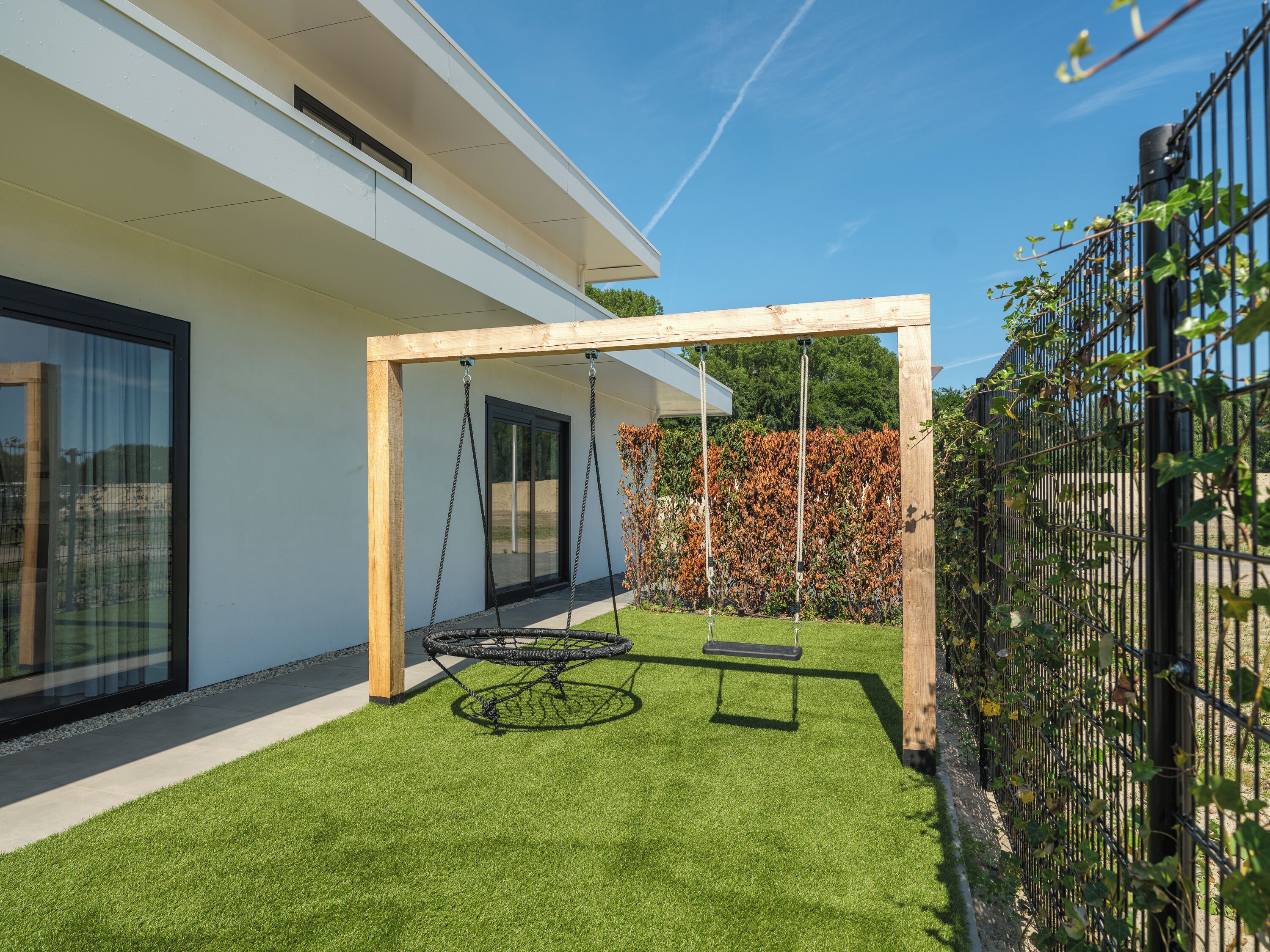 Een modern huis met een schommel en een omheinde tuin.