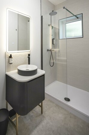Un baño moderno con un lavabo redondo, un espejo, ducha con cabina de vidrio y una ventana pequeña.