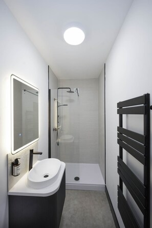 Un baño moderno con un lavamanos blanco, un espejo, una ducha y un toallero negro.