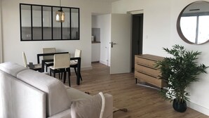 Ein modernes Wohnzimmer mit Sofa, Esstisch, Stühlen, einer Pendelleuchte, einem Spiegel und einem Blumentopf.