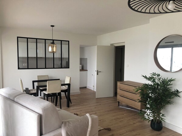 Ein modernes Wohnzimmer mit Sofa, Esstisch, Stühlen, einer Pendelleuchte, einem Spiegel und einem Blumentopf.