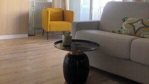 Ein modernes Wohnzimmer mit einer Couch, einem gelben Sessel, einem runden schwarzen Tisch mit einer dekorativen Vase, einem Deckenventilator und einem Fenster mit Vorhängen.
