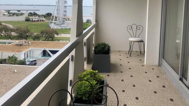 Ein Balkon mit Blick auf ein Riesenrad, einem Stuhl, Topfpflanzen und einem gefliesten Boden.
