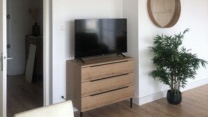 Ein modernes Wohnzimmer mit Flachbildfernseher auf einem Holzschrank, einer Pendelleuchte, einem runden Spiegel und einem Blumentopf.