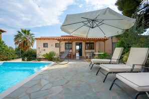 A poolside area with lounge chairs and an umbrella, a building with a tiled roof, and a clear sky. - Sea breeze maisonette sea view & pool (Koropi)