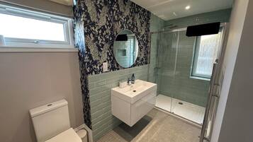 Et moderne badeværelse med toilet, vask med spejl og bruseniche.