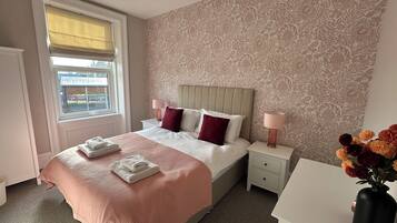 Een hotelkamer met een bed, bedlampen, een raam met uitzicht en een bloemenvaas.
