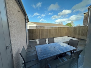 An outdoor patio with a table and chairs, a wooden fence, and a building in the background. - Abbotsford (Kelso)