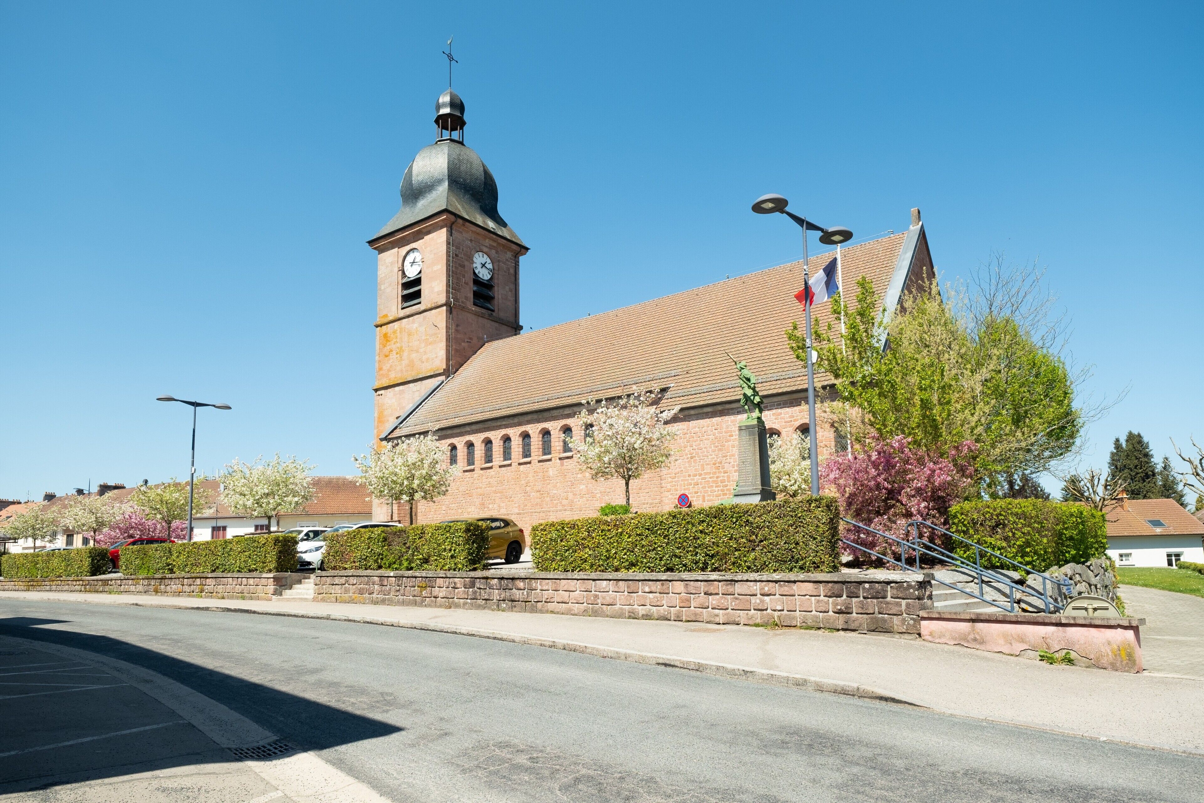 A church with a clock tower, a flag, and a statue in front.