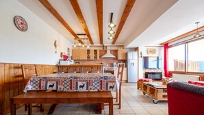 A cozy kitchen with wooden beams, a dining table with a patterned tablecloth, and a red sofa. - Apartment 'Les Airelles' with Mountain View, Private Terrace and Wi-Fi (La Bresse)