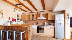 A kitchen with wooden beams, a bar area with stools, a refrigerator, and a microwave. - Apartment 'Les Airelles' with Mountain View, Private Terrace and Wi-Fi (La Bresse)