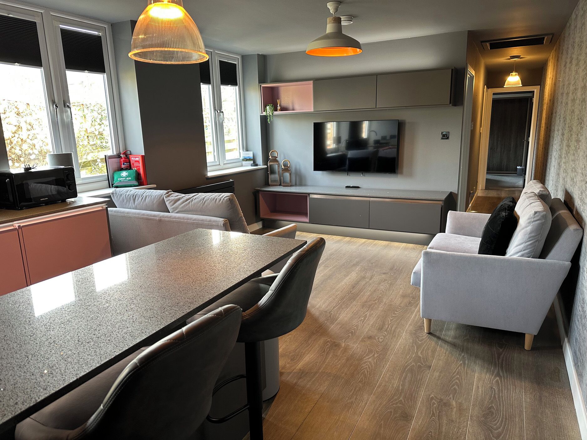 A modern kitchen with a dining area, a flat-screen TV mounted above the seating area, and a large window providing natural light.