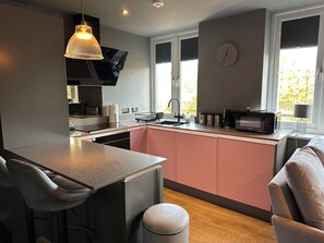 A modern kitchen with a central island, a built-in oven, and a window with a view. - The Tay (Melrose)