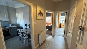 A hallway with a kitchen on the left, a dining area with chairs, and a radiator on the wall. - The Tweed (Melrose)