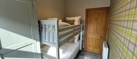 A small, compact room with bunk beds, a wardrobe, a door, and a radiator.