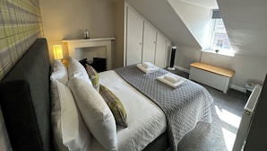 A bedroom with a bed, bedside tables, a desk, a radiator, and a window with a view. - The Tweed (Melrose)