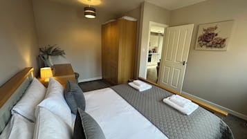A hotel room with a bed, bedside table, lamp, wardrobe, and a door leading to a bathroom.