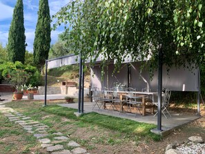 Une terrasse extérieure avec une table et des chaises, entourée de verdure et de chemins en pierre.