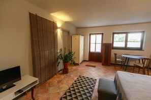 A room with a television, a potted plant, a dining table with chairs, and a door leading to another room.
