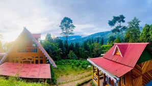 A traditional wooden house with a red roof, surrounded by lush greenery and hills. - Ganganiwas Homestay Sonada (Darjeeling)