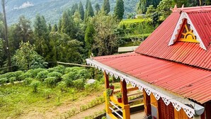 A traditional house with a red roof, surrounded by lush greenery and hills. - Ganganiwas Homestay Sonada (Darjeeling)