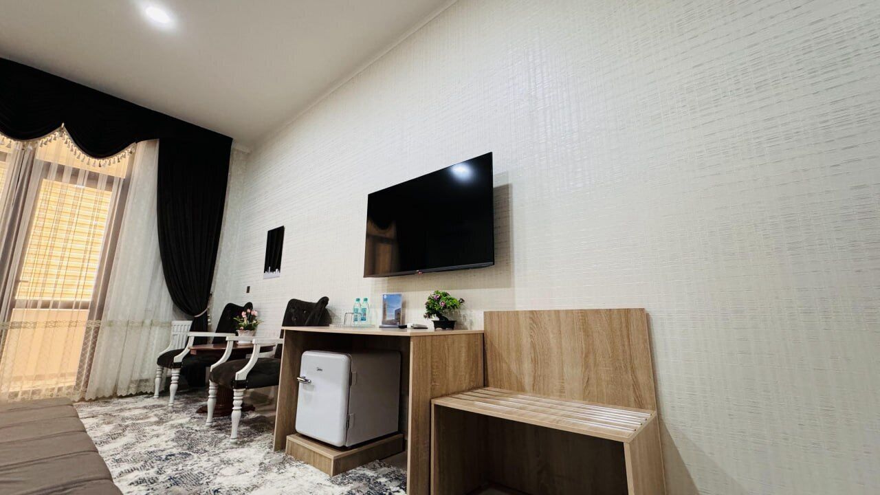 Uma sala de estar moderna com uma televisão de tela plana, um refrigerador pequeno, um banco de madeira e uma área de jantar com cadeiras e mesa.