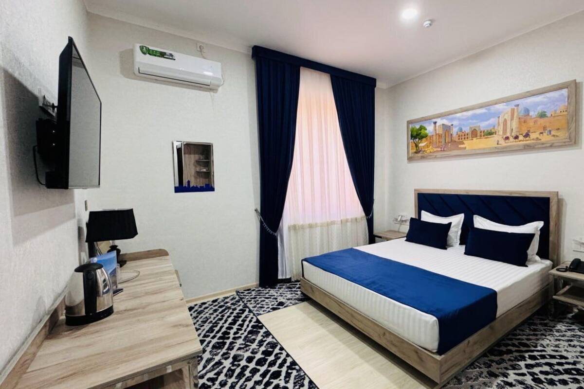 Quarto de hotel com cama, escrivaninha, cadeira, televisão, ar condicionado, quadro e chão estampado.