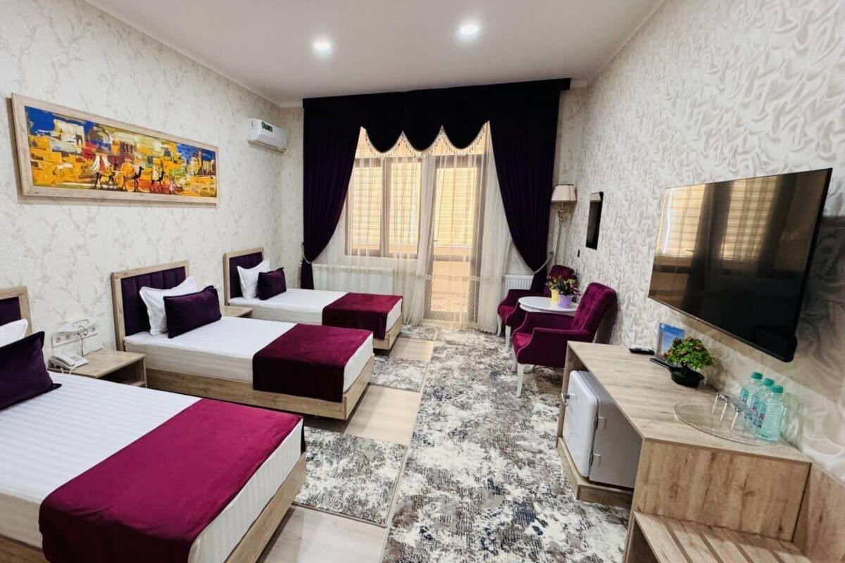 Quarto de hotel com três camas, uma TV, uma escrivaninha e uma cadeira.