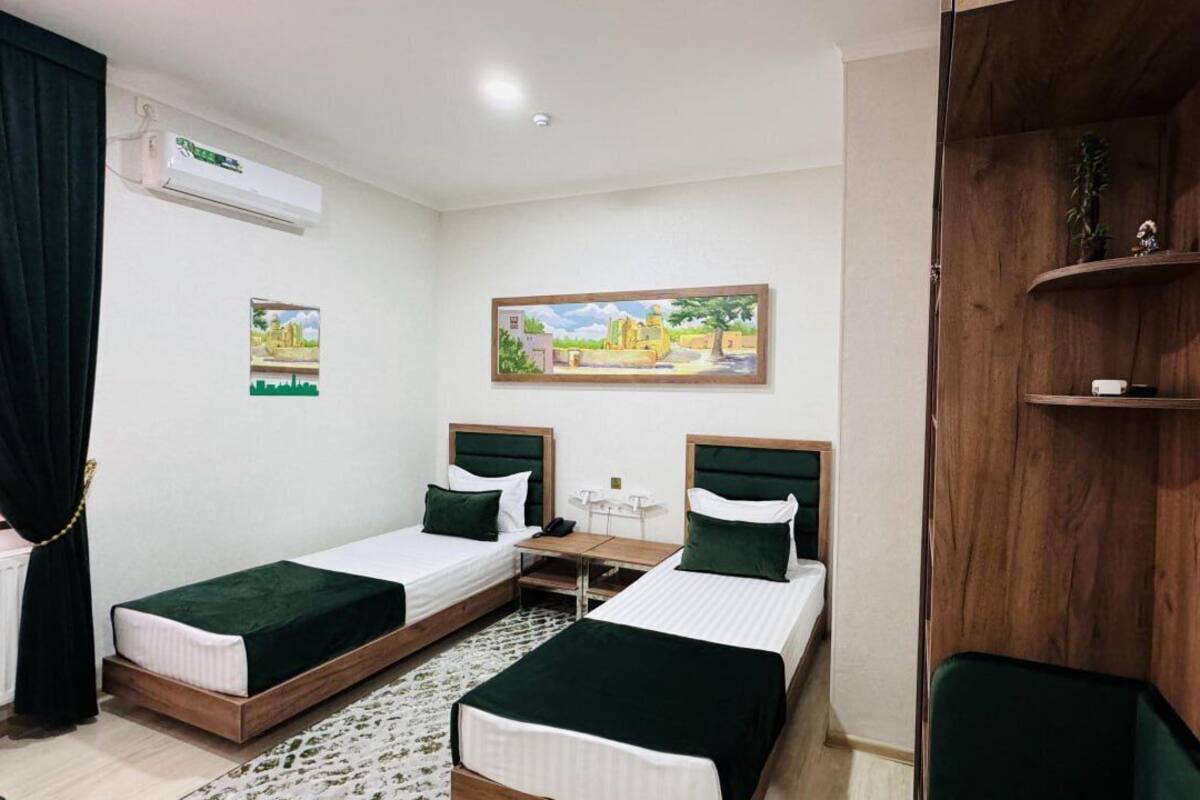 Quarto de hotel com duas camas de solteiro, uma mesinha, unidade de ar condicionado e uma prateleira de madeira com objetos decorativos.