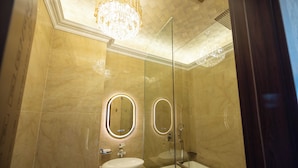 Un baño moderno con un espejo ovalado grande, un lavamanos y una ducha con cerramiento de vidrio.