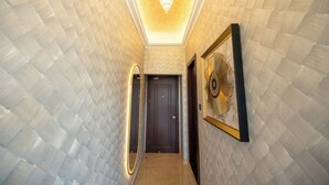 Un pasillo con un papel tapiz estampado, un candelabro, una puerta y un cuadro enmarcado.
