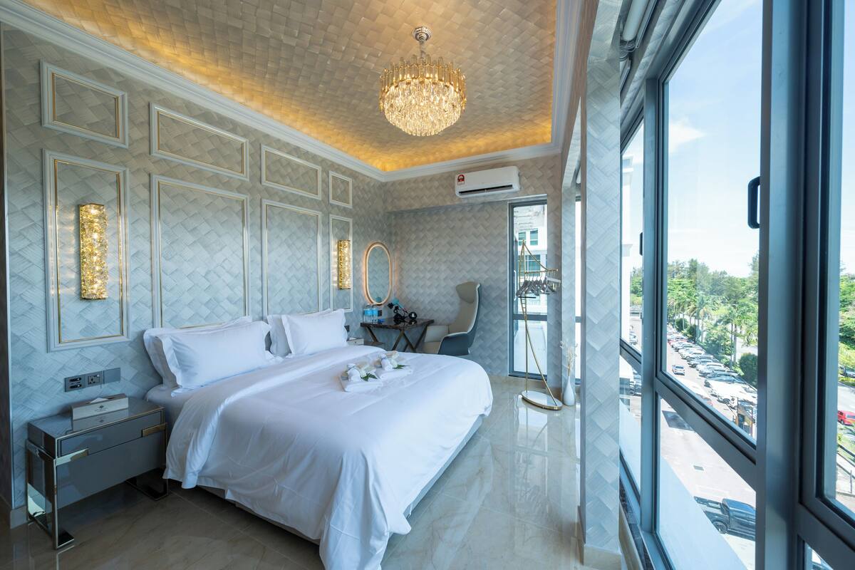 Quarto de hotel moderno com cama grande, lustre, vista da cidade e varanda.
