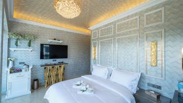 Ein modernes Hotelzimmer mit einem großen Bett, einem Flachbildfernseher, einem Holfnachtkästchen und einer Kristallleuchtre.