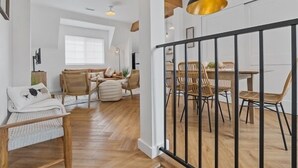 Een ruime kamer met houten vloer, een eethoek met stoelen en tafel, en een bed met een witte hoofdbord.
