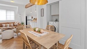 Een moderne keuken met witte kastjes, een eethoek met een houten tafel en stoelen, en een grote hanglamp.