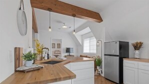 Een keuken met een houten aanrecht, witte kasten, een roestvrijstalen koelkast en een dakraam.