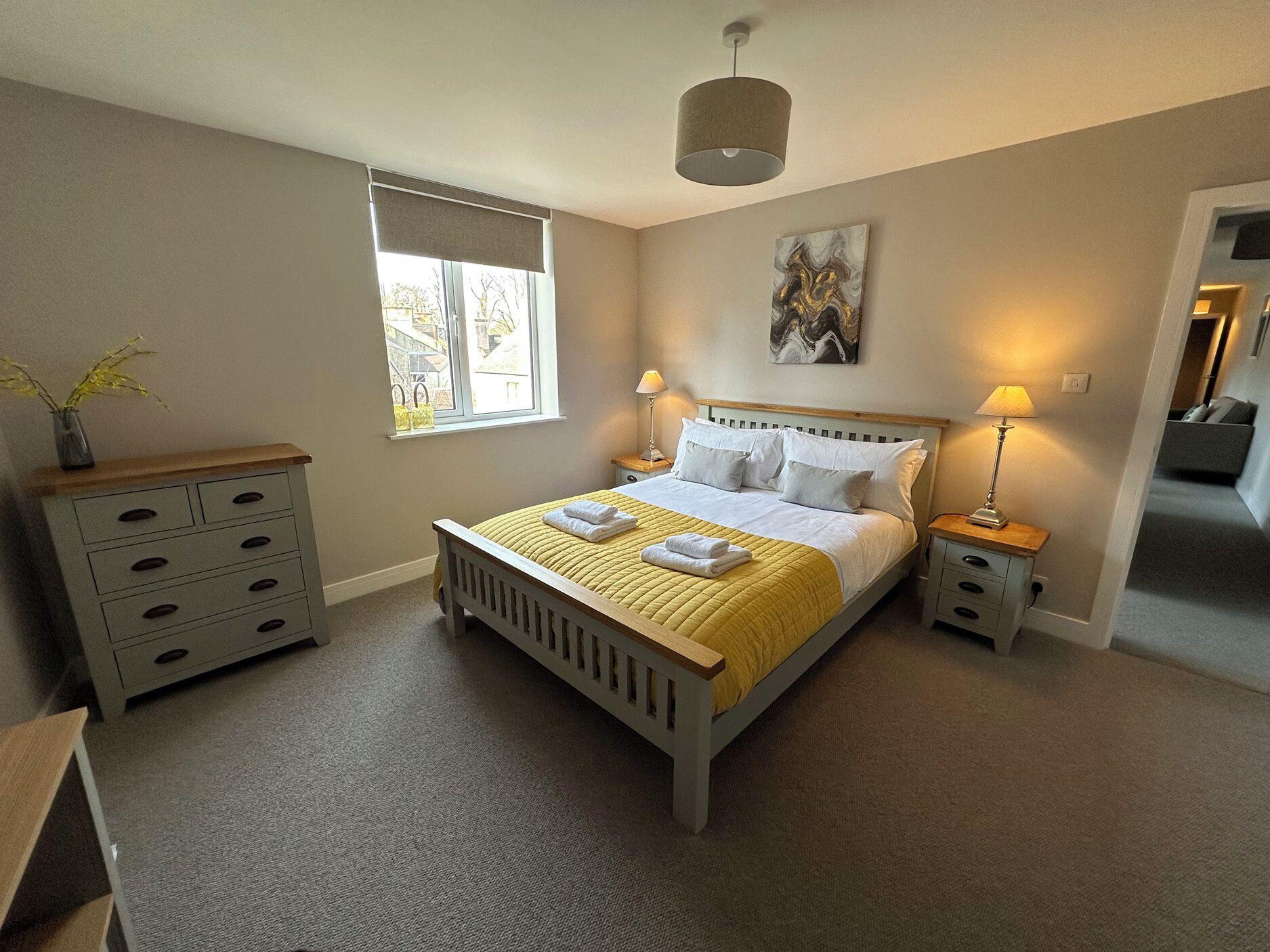 A bedroom with a bed, bedside tables, a window, a lamp, a painting, and a dresser.
